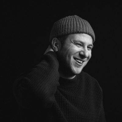 Oli Rockberger, wearing a beanie, smiling in black and white photograph